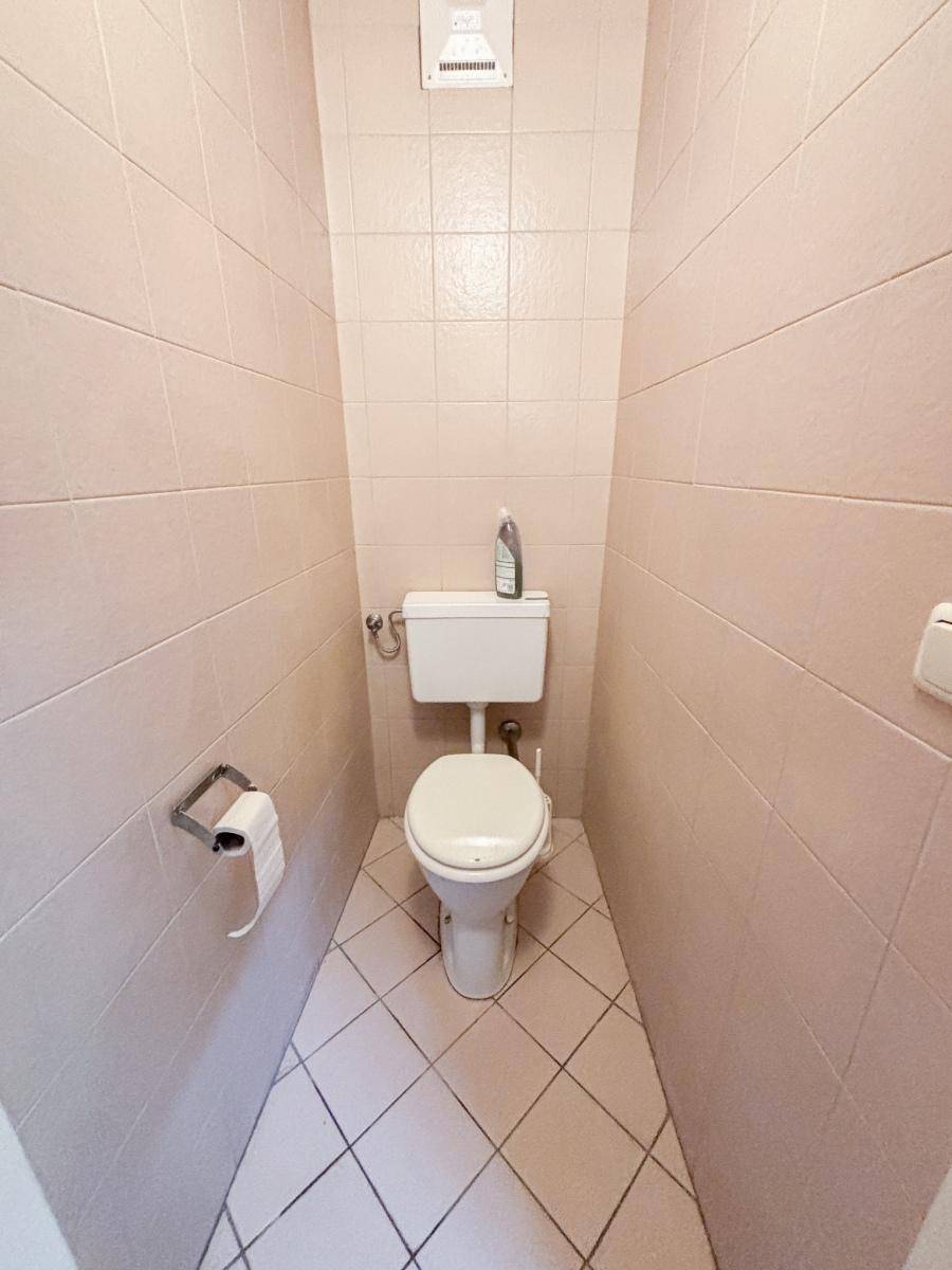 Kleiner Toilettenraum mit beigefarbenen Fliesen an Wänden und Boden sowie einer einfachen Toilette.