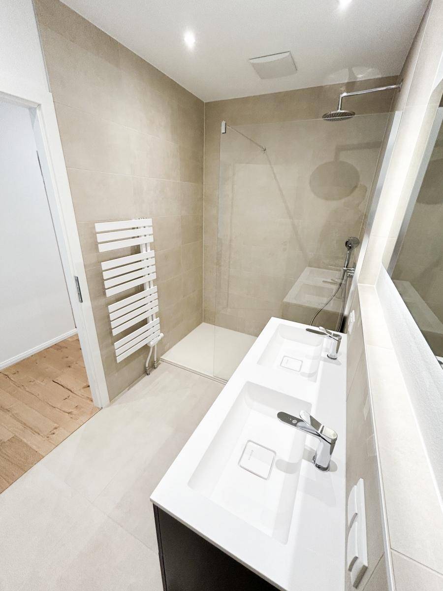Elegantes Badezimmer mit begehbarer Dusche, Doppelwaschbecken und modernem Handtuchheizkörper.