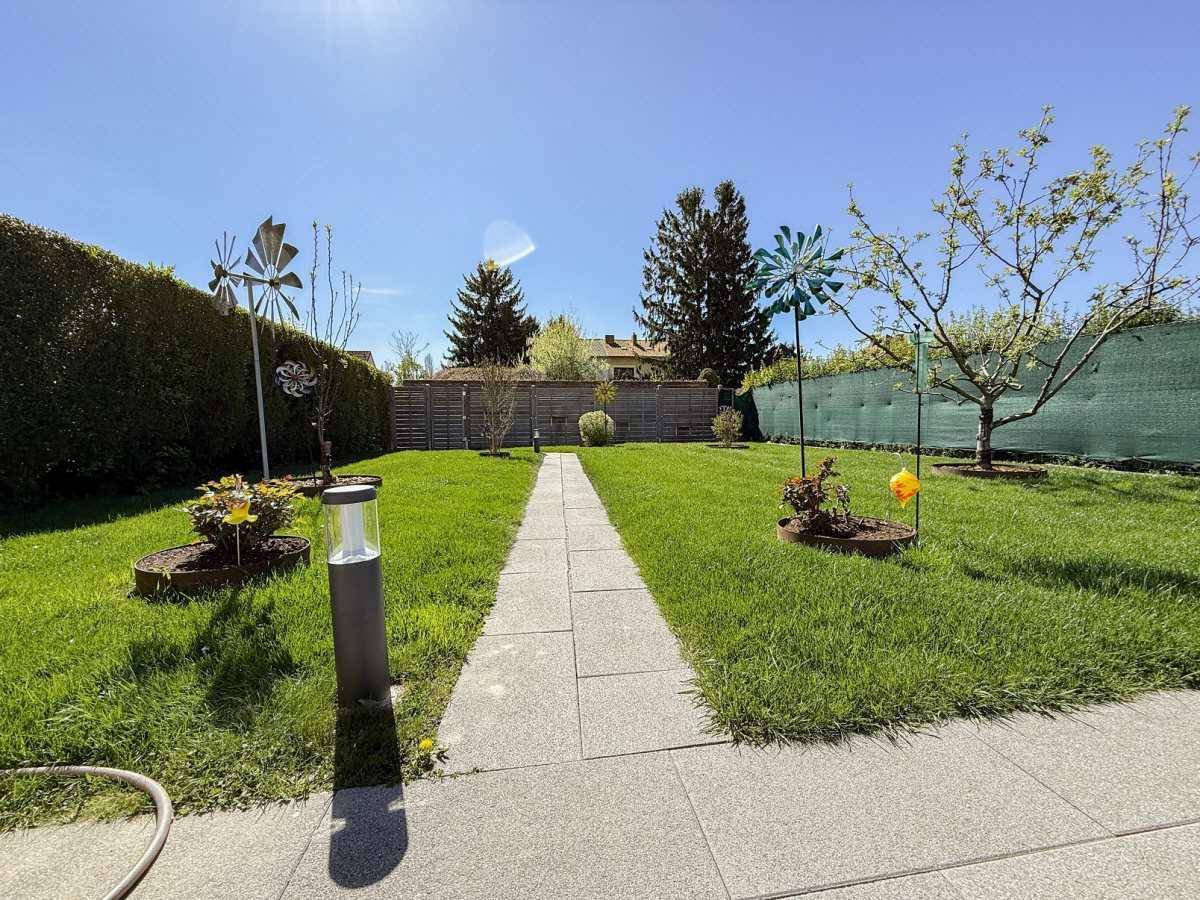 Gerader Steinweg führt durch den grünen Rasen des sonnigen Gartens mit seitlichen Beeten.
