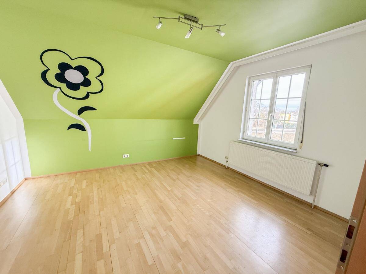 Heller Raum im Dachgeschoss mit Holzdielenboden, Dachschräge und auffälliger grüner Decke.