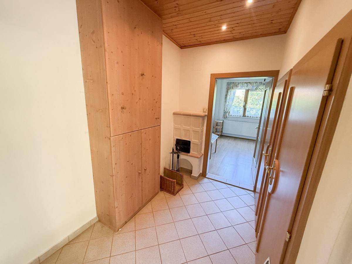 Eingangsbereich mit Holzschrank, gefliestem Boden und Blick auf einen weiteren Kachelofen.