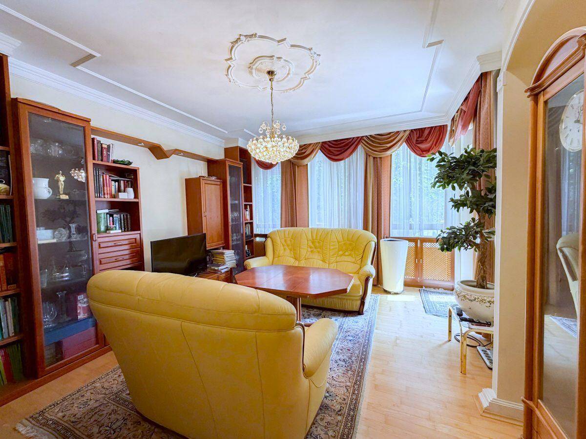 Gemütliches Wohnzimmer mit gelben Sofas, Parkettboden und einem Kronleuchter an der Stuckdecke.