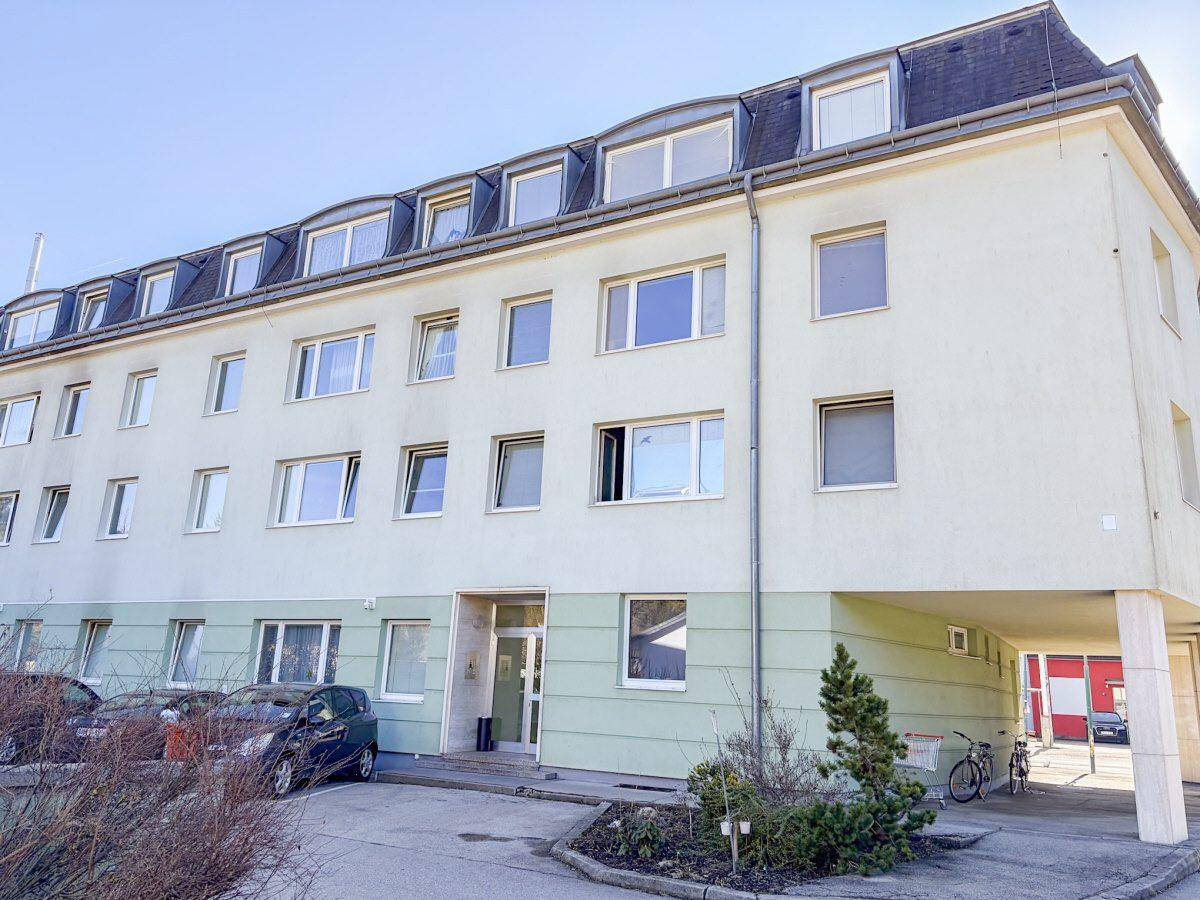Gebäudefassade mit vielen Fenstern, dem Eingang und einem überdachten Bereich im Erdgeschoss.