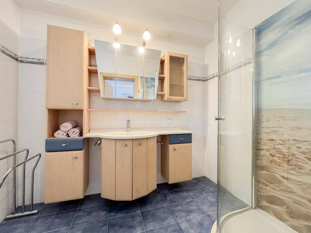 Funktionales Badezimmer mit Duschkabine, Einzelwaschbecken und blauen Bodenfliesen.