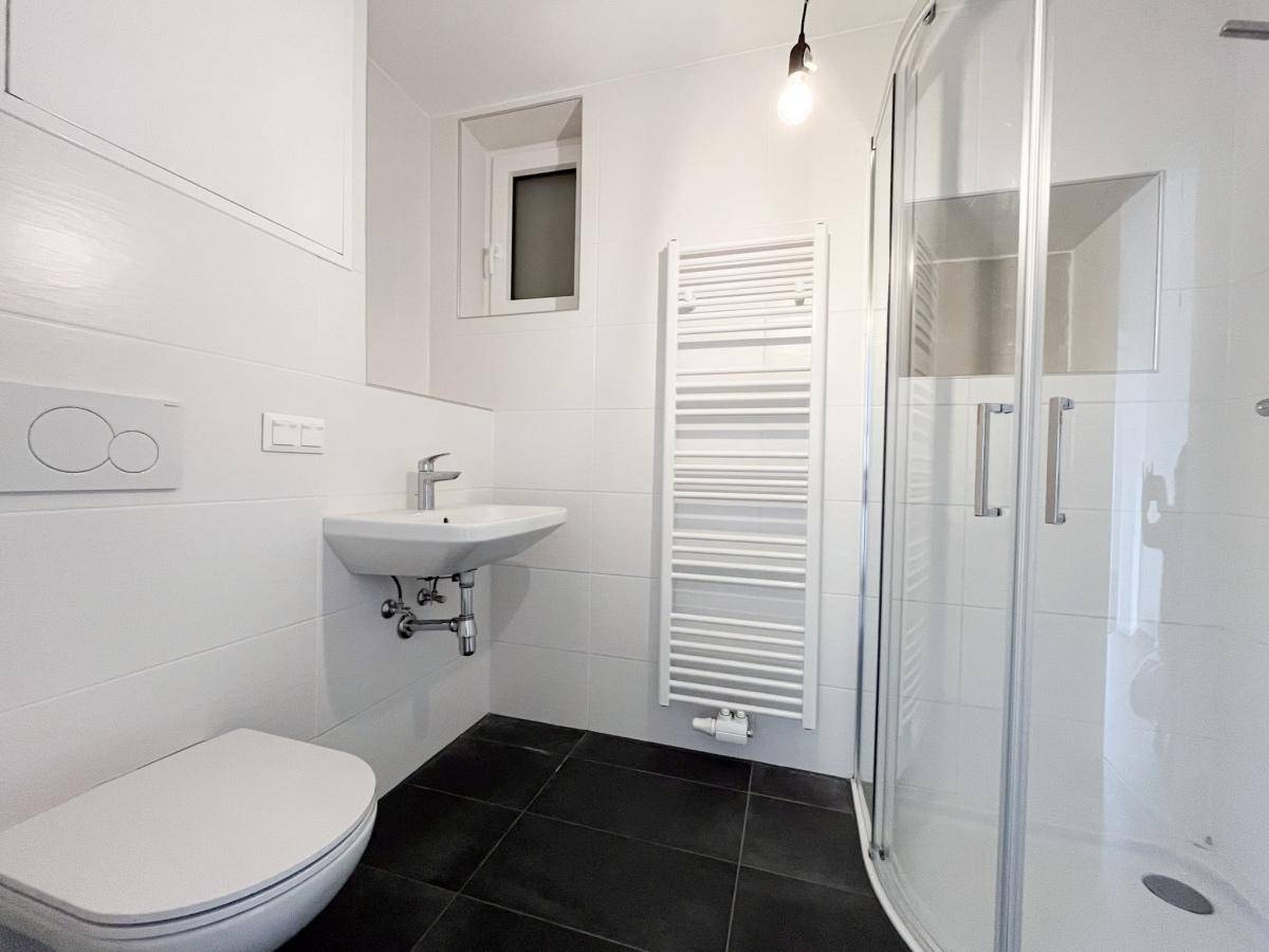 Modernes Badezimmer mit weißen Fliesen, schwarzem Boden, Dusche und beheiztem Handtuchhalter.
