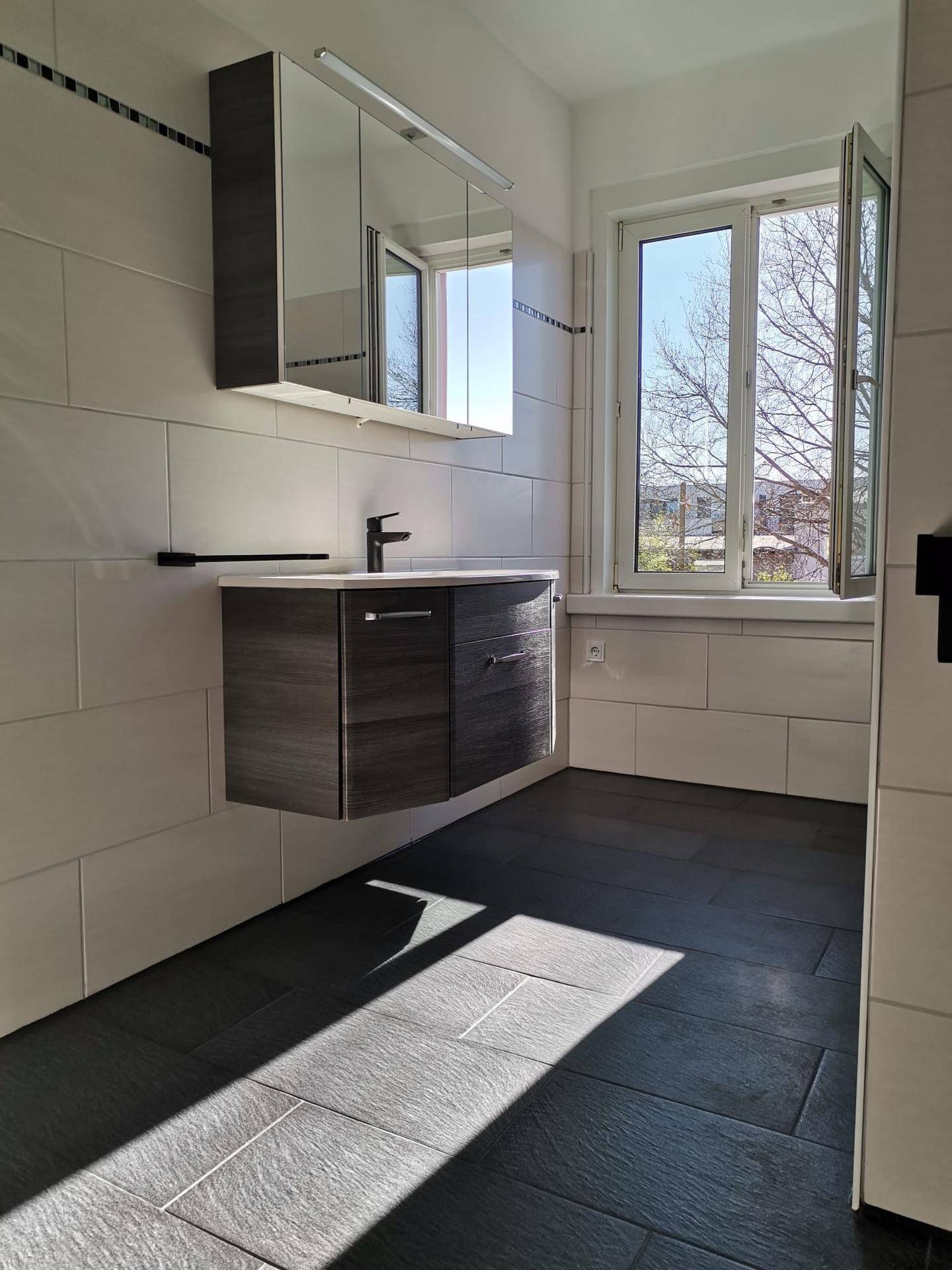Helles Badezimmer mit modernem Waschtisch, Spiegelschrank und Fenster für Tageslicht.