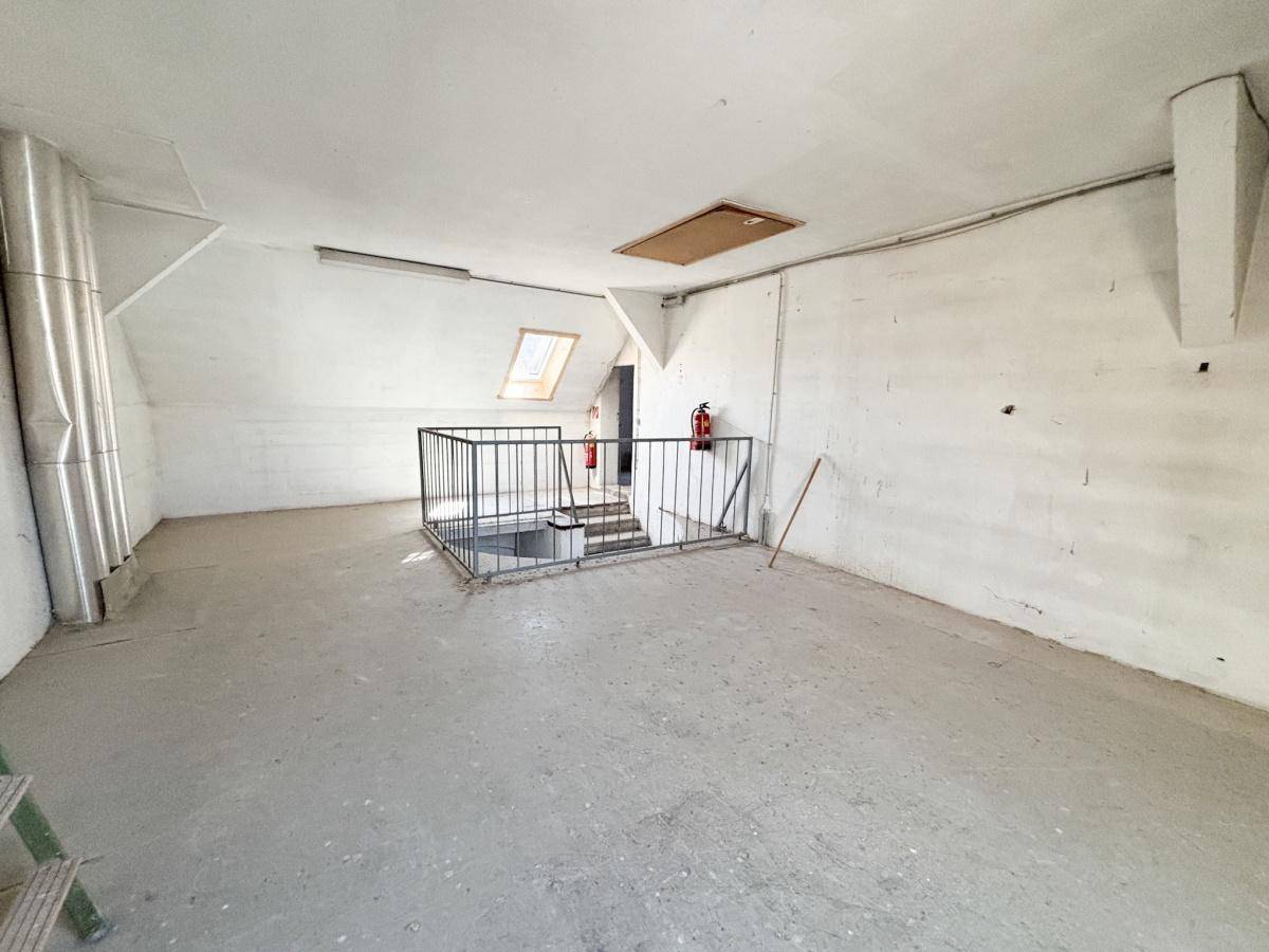 Großer, leerer Dachbodenraum mit schrägen Wänden, Betonboden und Dachfenstern.