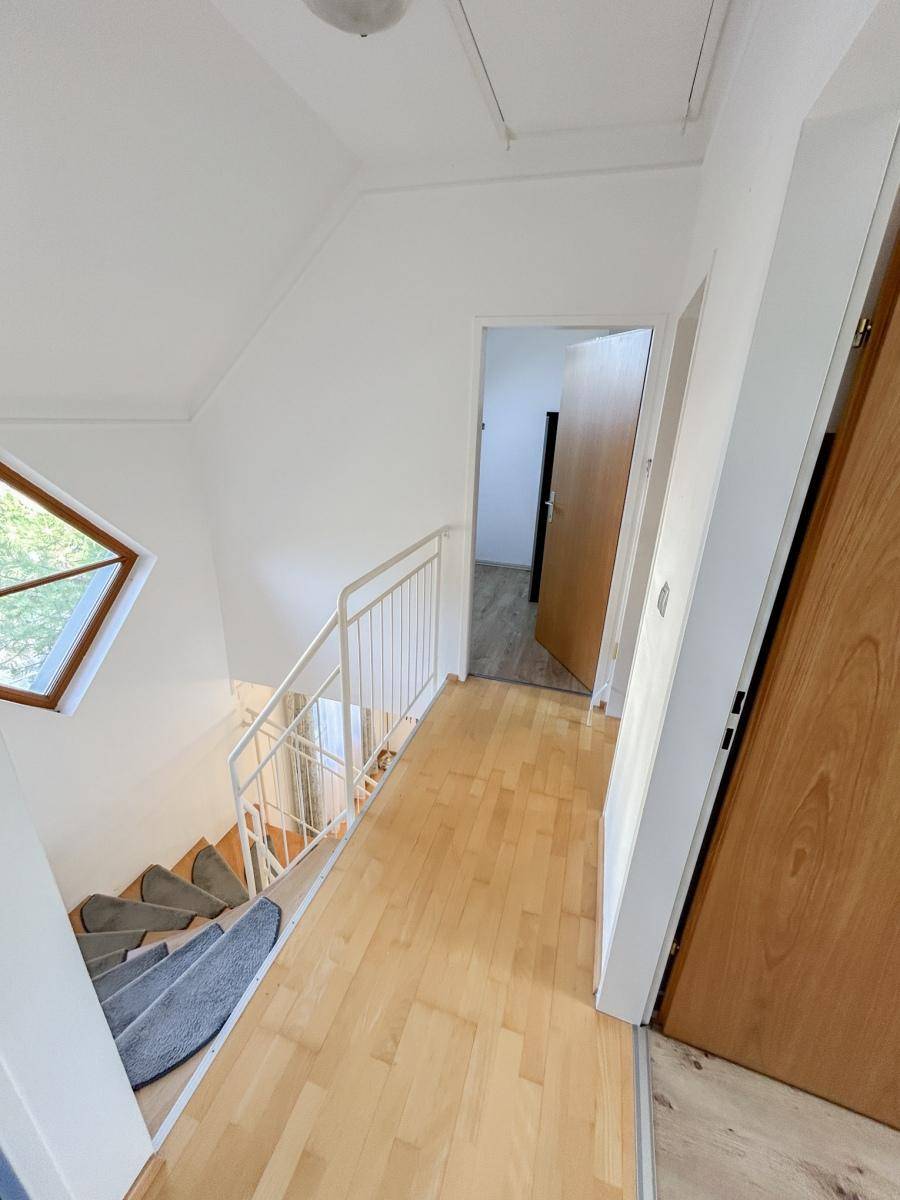 Heller Flur mit Holztreppe und Zugang zu weiteren Räumen im Obergeschoss.