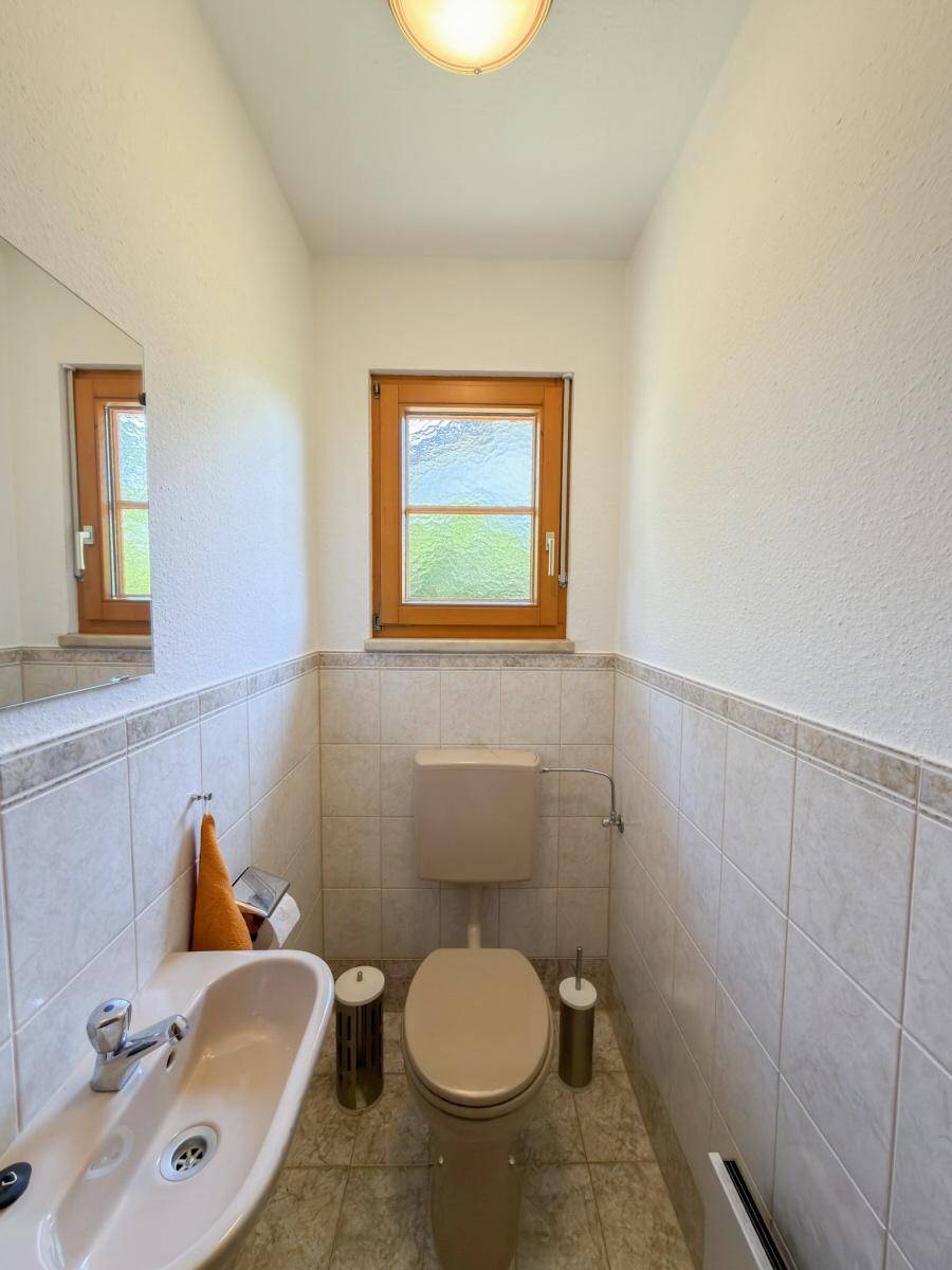 Separate Toilette mit Fenster, Waschbecken und beigefarbenen Fliesen.