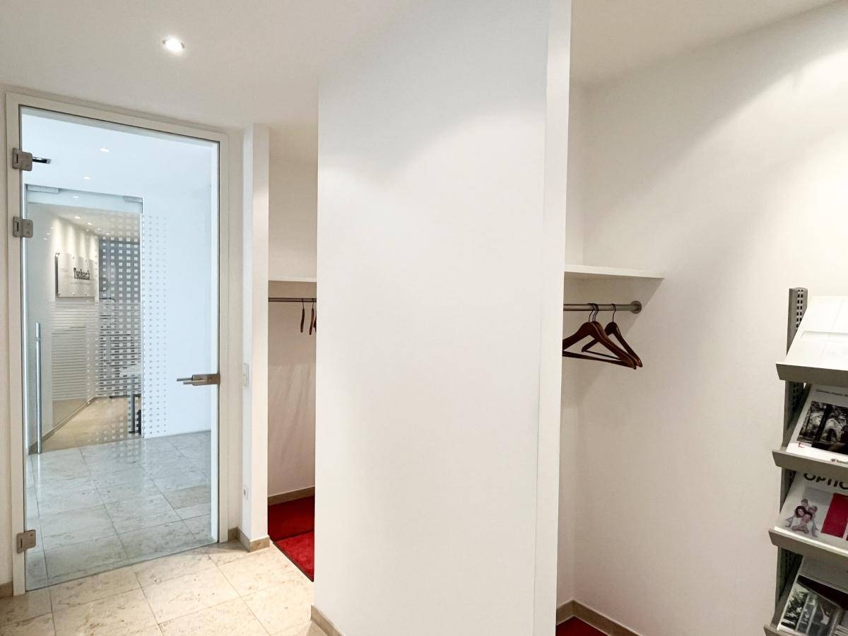 Eingangsbereich mit Garderobe, Fliesenboden und Glastür zu den Büroräumen, praktisch und hell gestaltet.