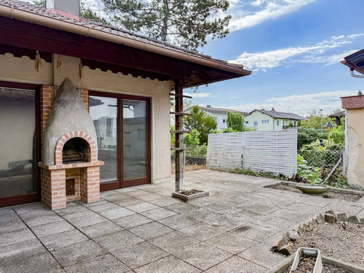 Große gepflasterte Terrasse mit gemauertem Grill und Blick ins Grüne.