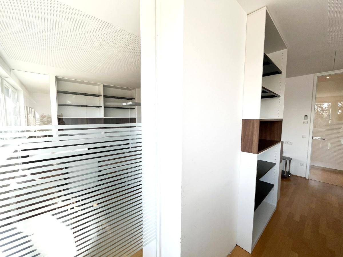 Moderner Bürobereich mit Glastür, Holzfußboden und integrierten Regalsystemen, schafft eine offene Arbeitsumgebung.