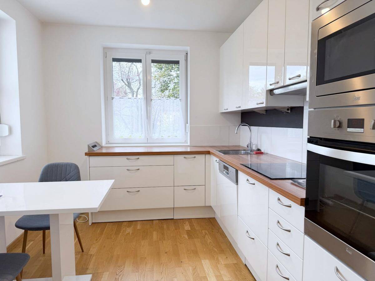 Moderne Küche mit weißen Hochglanzfronten, Holzarbeitsplatte und Fensterblick.
