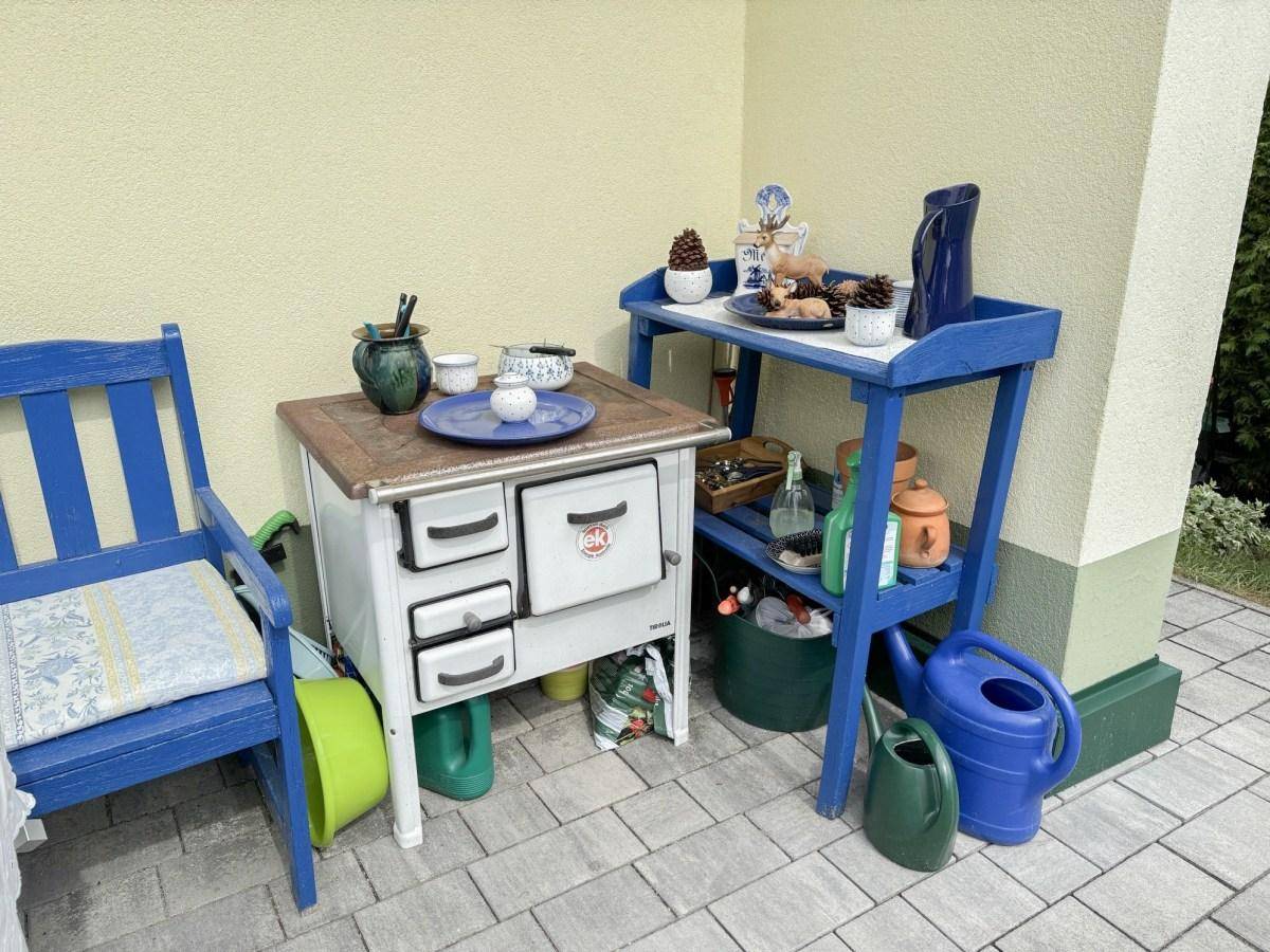 Detailansicht der Terrasse mit einem dekorativen alten Ofen und blauen Gartenmöbeln.
