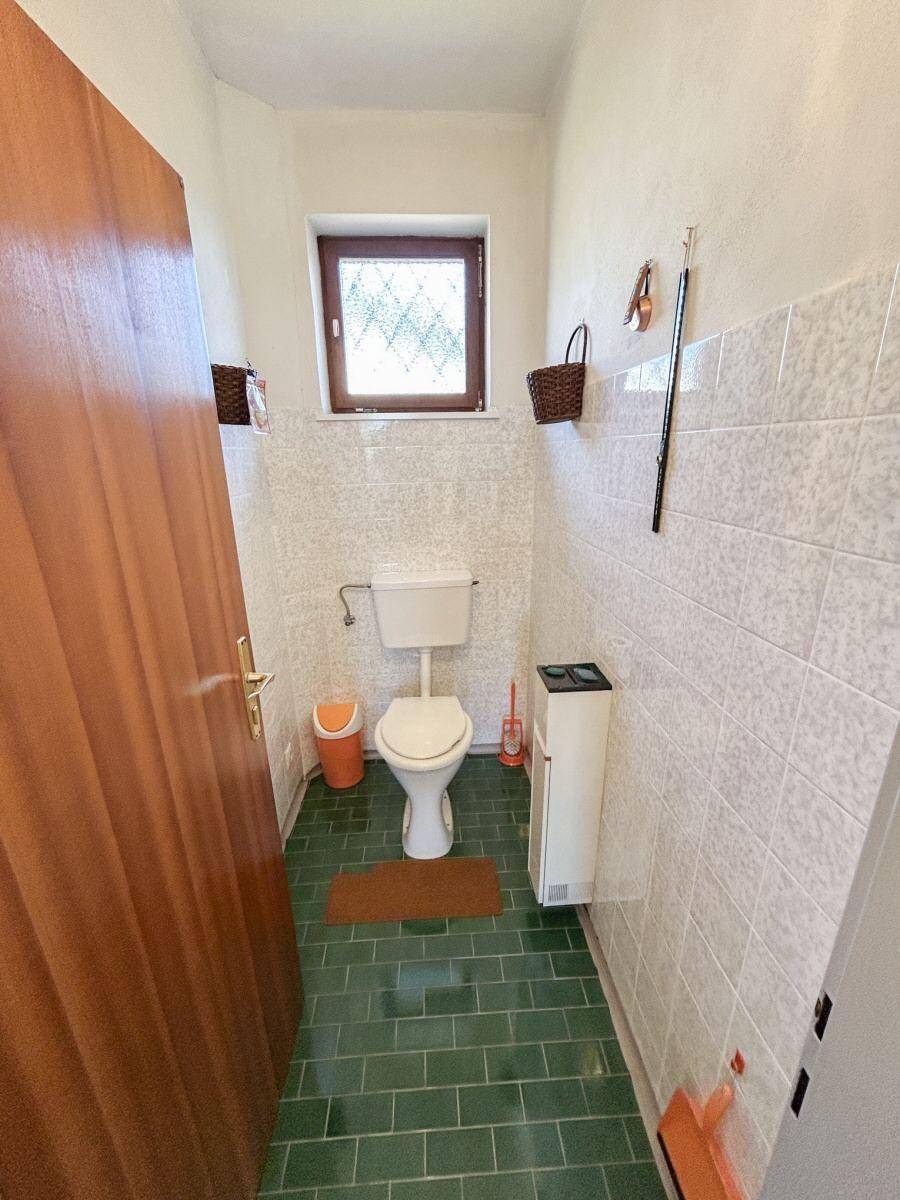 Separates WC mit grünen Bodenfliesen und einem kleinen Fenster.