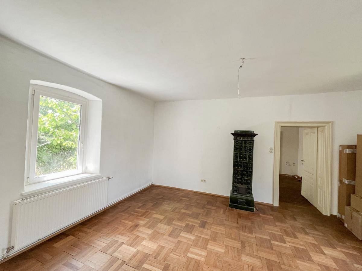 Helles Zimmer mit Parkettboden und einem traditionellen gusseisernen Ofen.