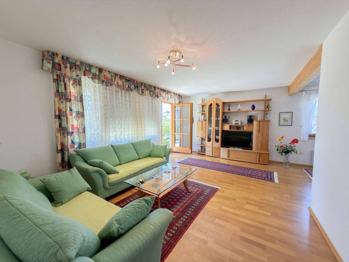 Geräumiges Wohnzimmer mit Holzboden, grünen Sofas und Blick ins Grüne.