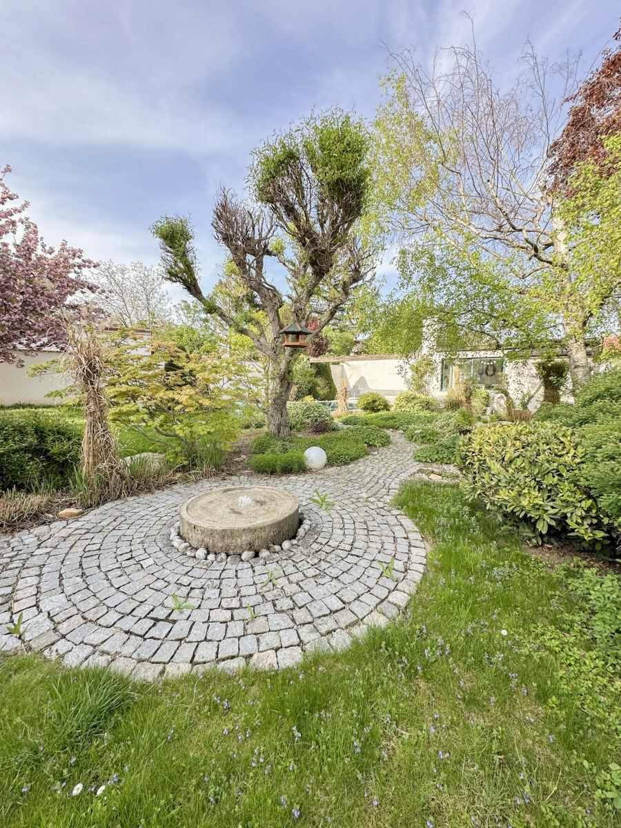 Malerischer Gartenweg aus Kopfsteinpflaster mit einem dekorativen Brunnen und üppiger Bepflanzung.