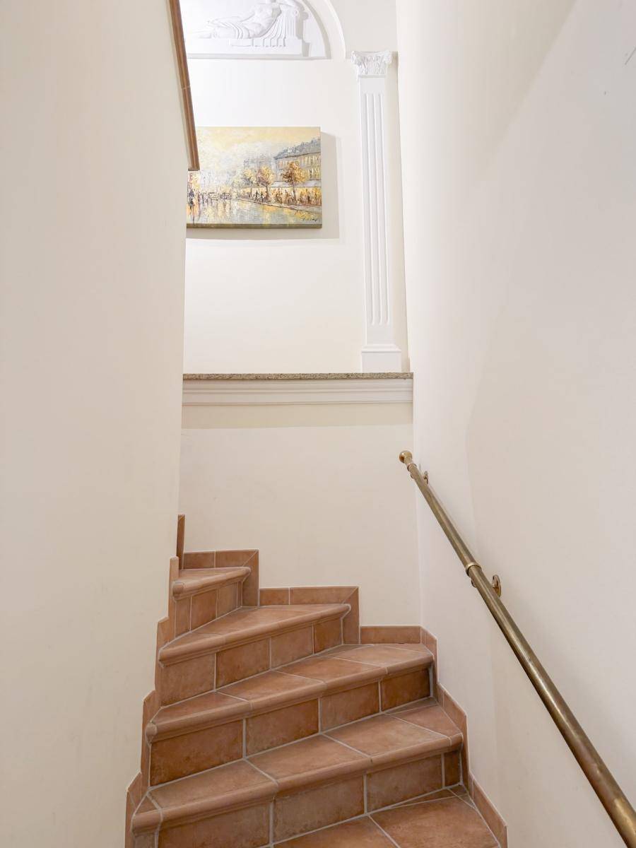 Treppenhaus mit Terrakotta-Stufen, elegantem Geländer und klassischer Stuckverzierung an der Wand.