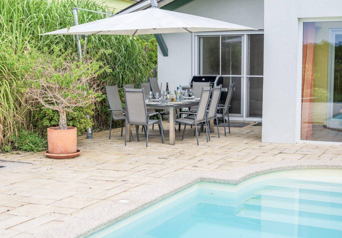 Gemütlicher Essbereich im Freien mit großem Sonnenschirm, Grill und direktem Zugang zum Pool.
