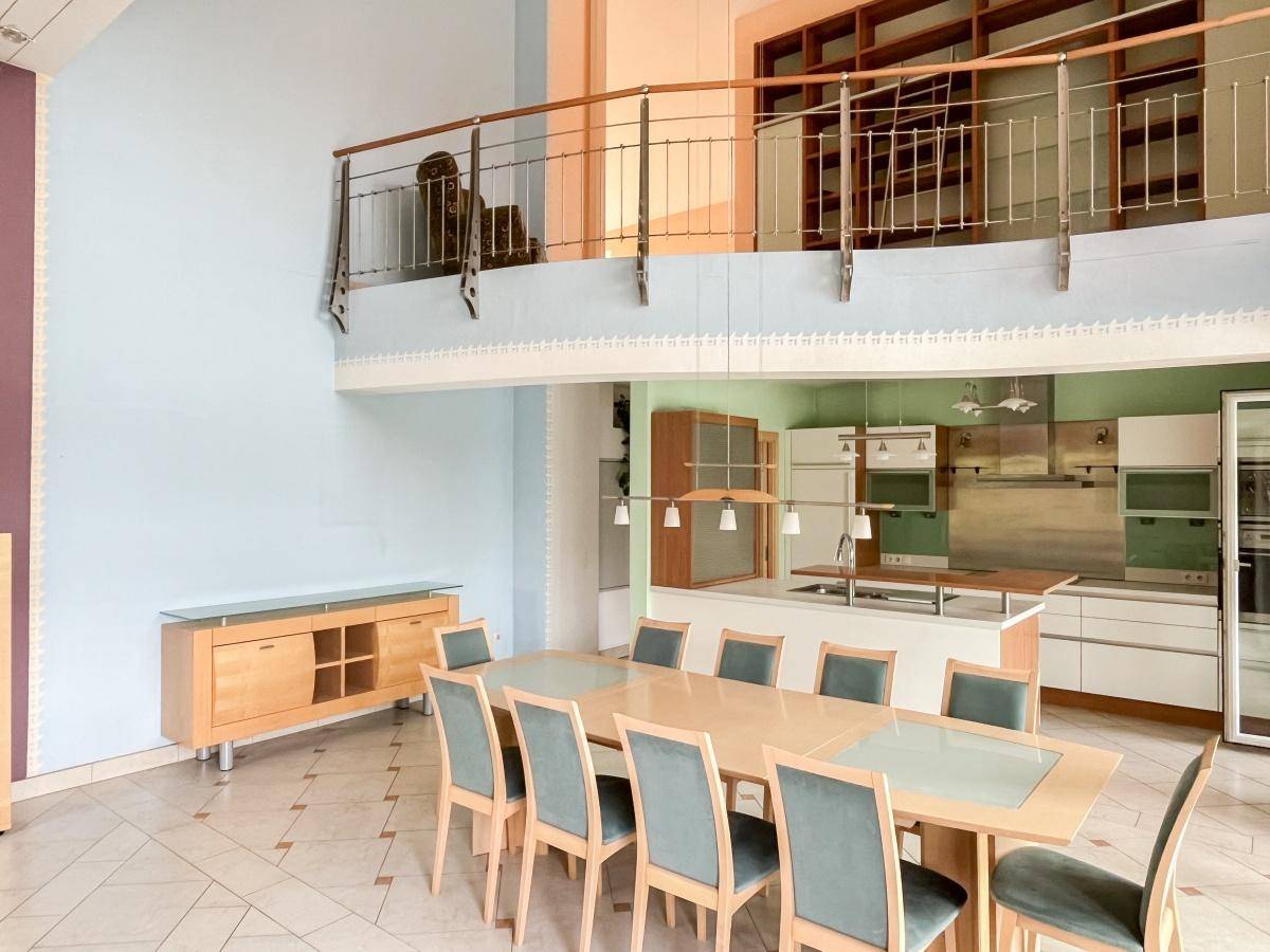 Geräumiger Essbereich mit großem Tisch, offener Küche und Blick auf die Galerie im Obergeschoss.