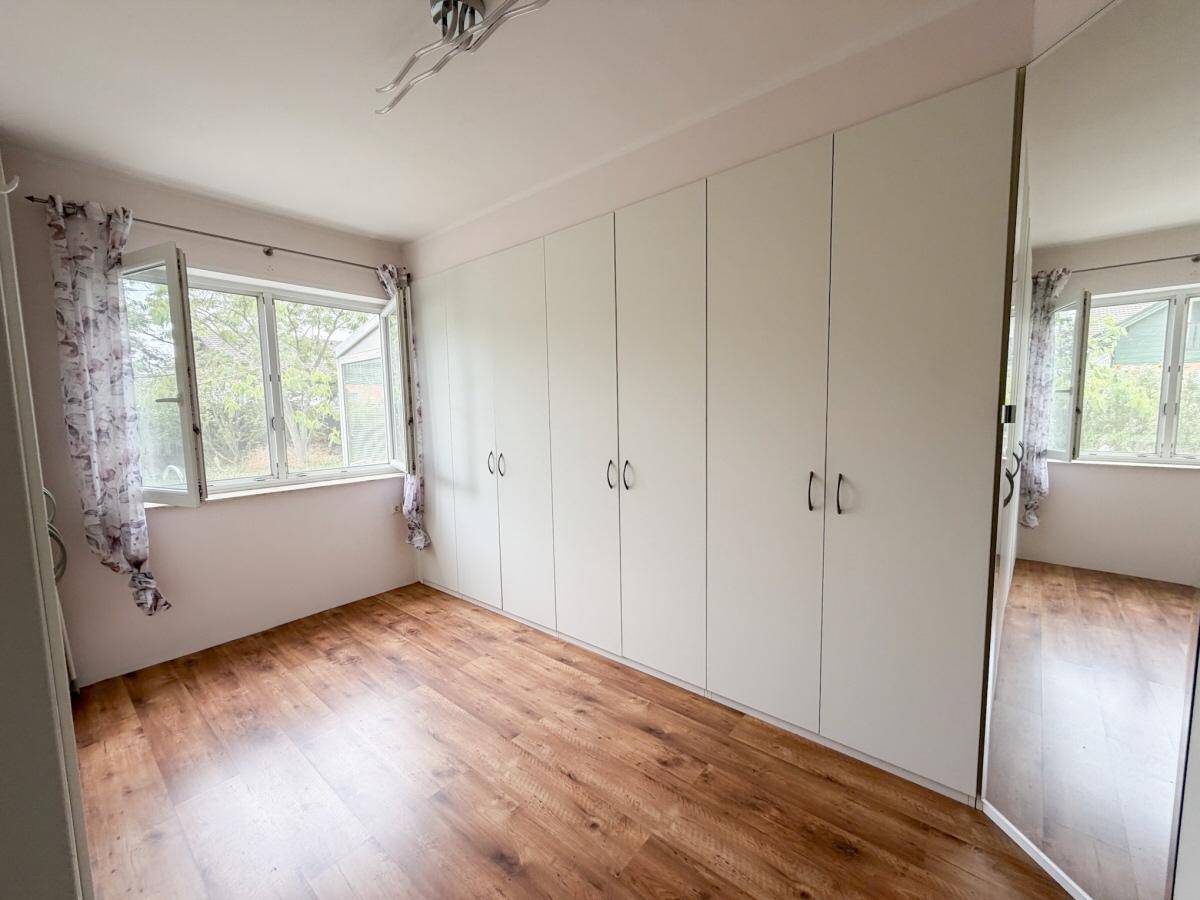 Schlafzimmer mit Einbauschränken, Laminatboden und Fenstern mit Blick nach draußen.
