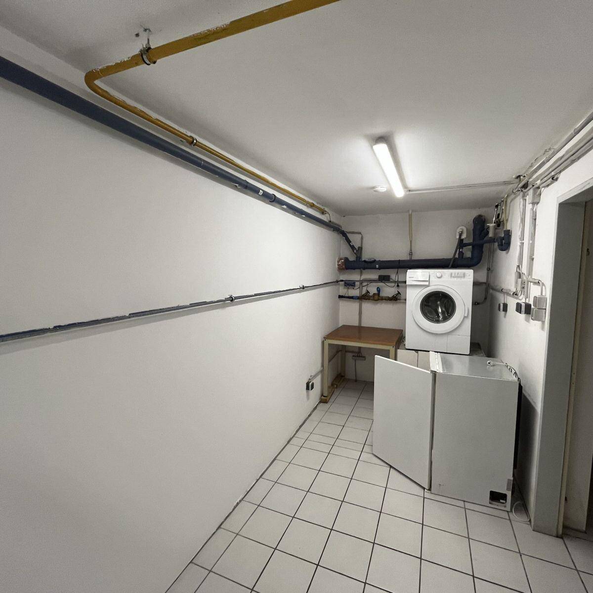 Waschküche im Keller mit Waschmaschine, Trockner und Fliesenboden, funktional eingerichtet.