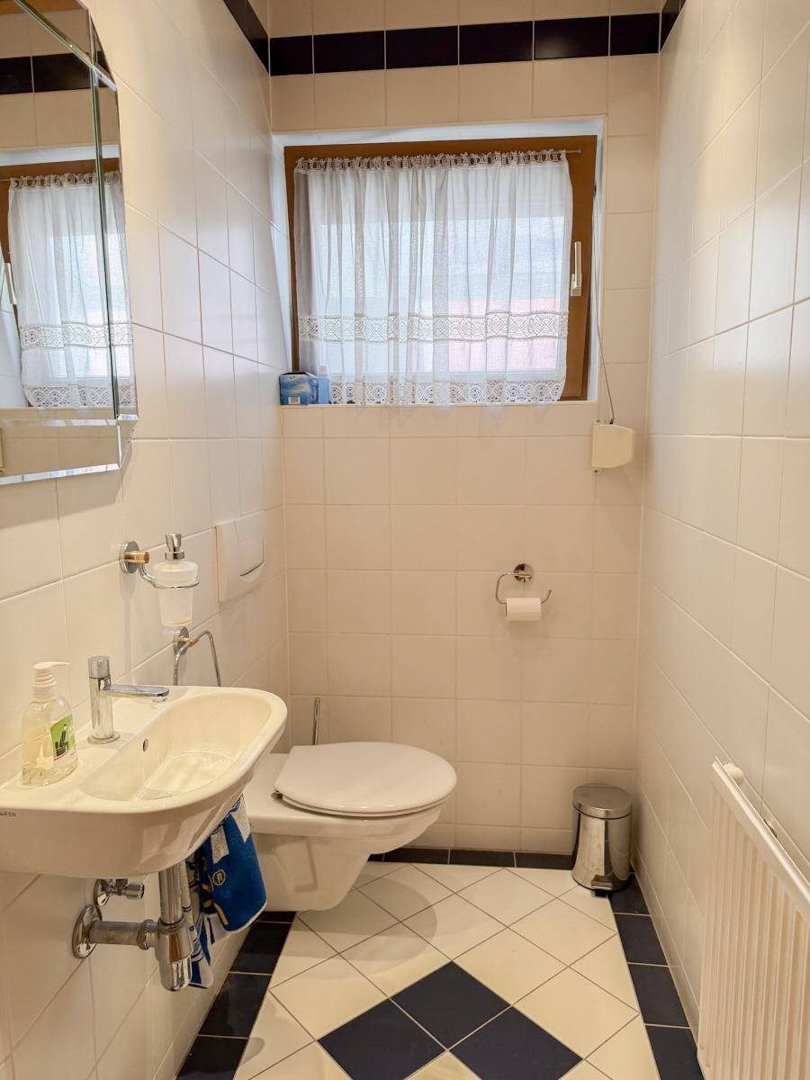Kleines Gäste-WC mit weißen Fliesen, dunklen Akzenten und einem Fenster für Tageslicht.