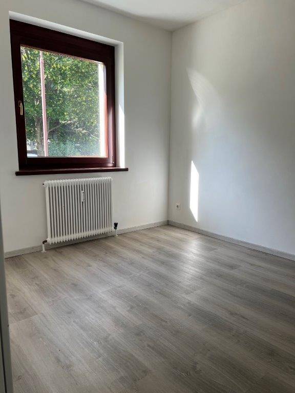 Helles Zimmer mit Laminatboden und einem Fenster, das viel Tageslicht hereinlässt.