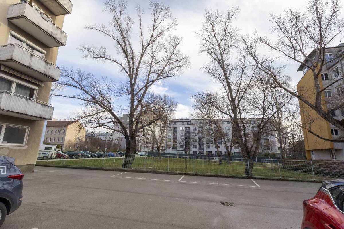 Außenansicht mit Parkplätzen, Bäumen und umliegenden Wohngebäuden in der Nachbarschaft.