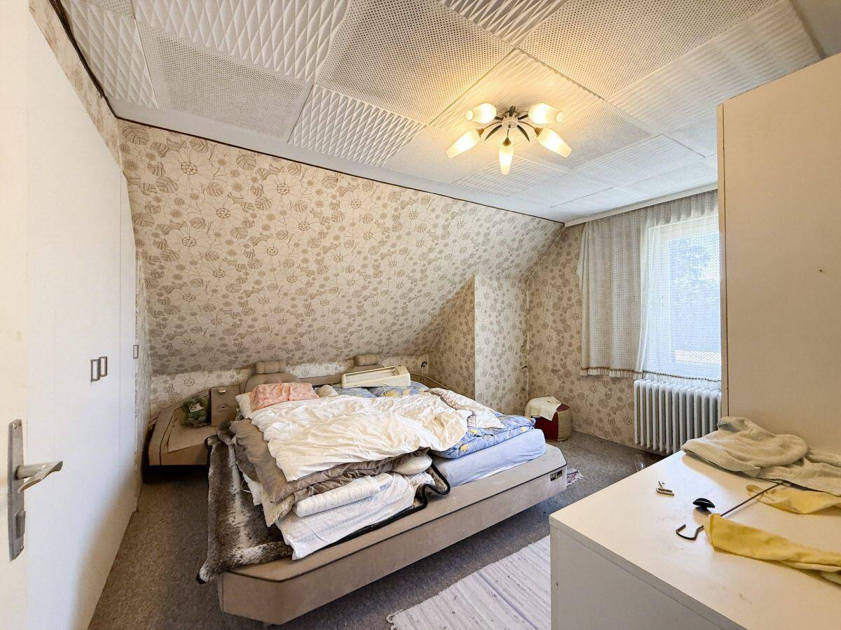 Dachgeschoss-Schlafzimmer mit floraler Tapete, Teppichboden und schrägen Wänden.