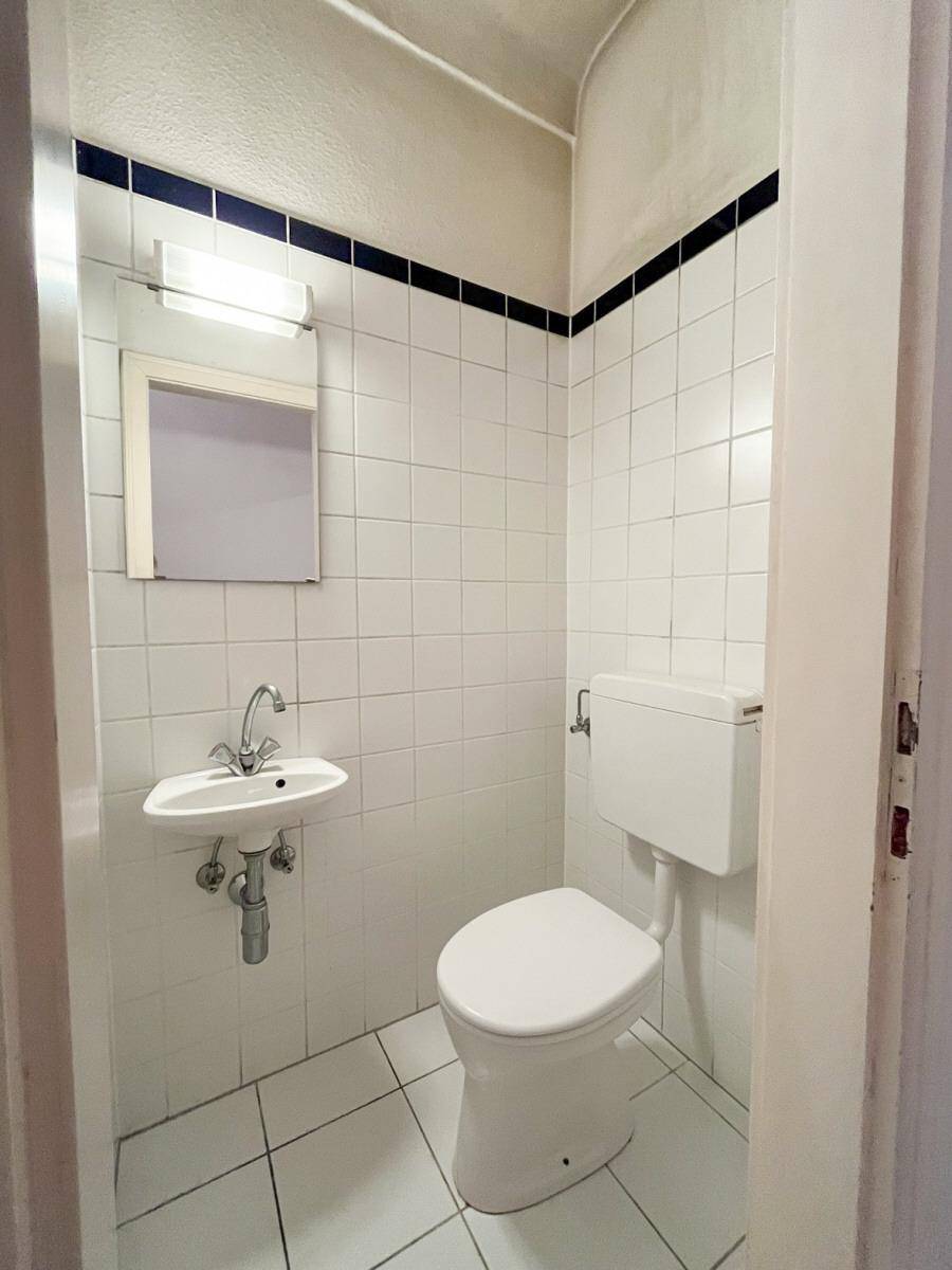 Kleines Gäste-WC mit weißen Fliesen, einem Waschbecken und einer Toilette, akzentuiert durch eine blaue Bordüre.