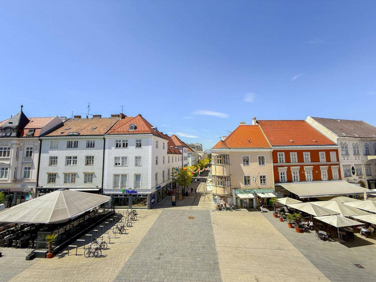 Blick über einen belebten Stadtplatz mit historischen Gebäuden und zahlreichen Cafés.