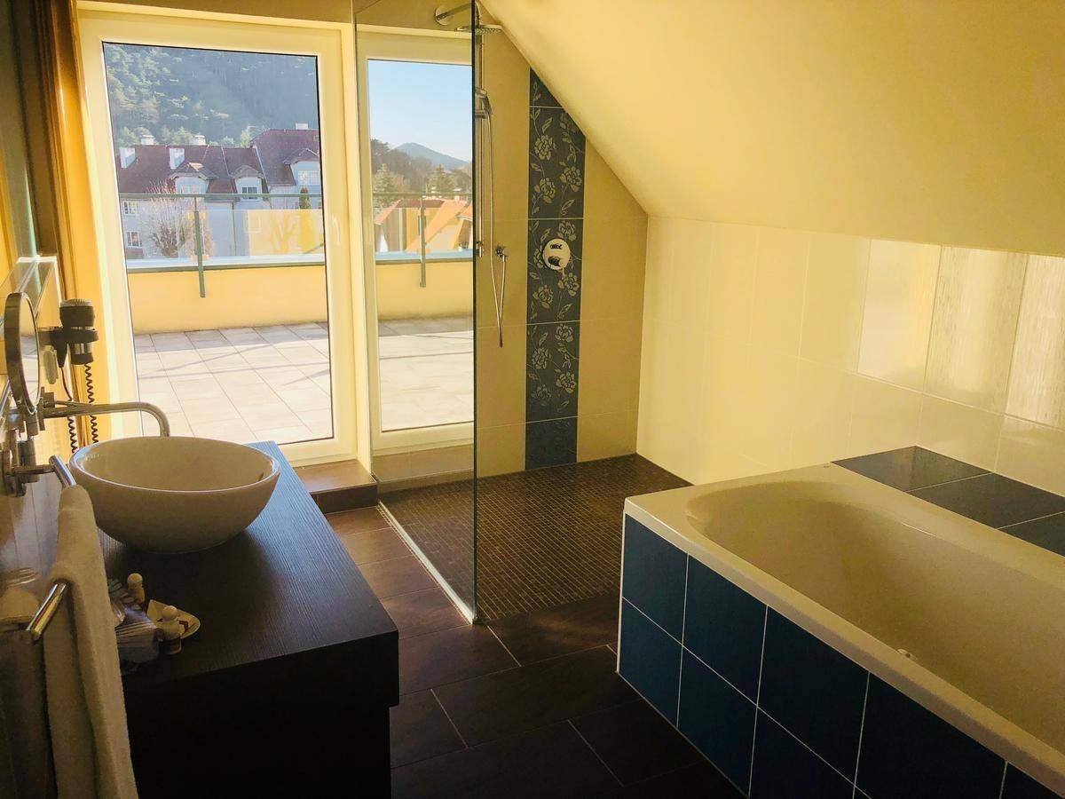 Helles Badezimmer mit Badewanne, Dusche und direktem Zugang zu einer sonnigen Terrasse.