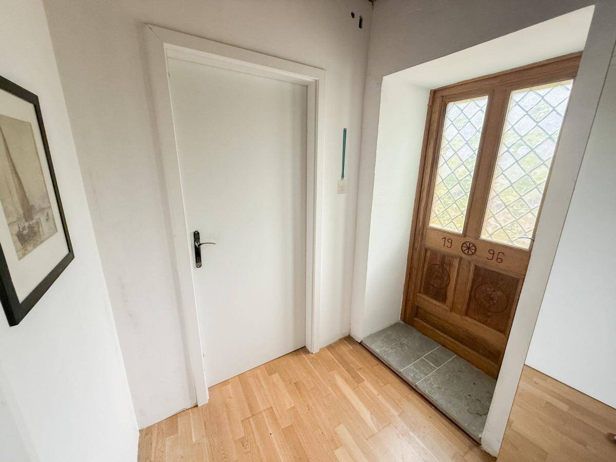 Heller Flur mit weißer Tür und einer rustikalen Holzeingangstür mit Glasfeldern.