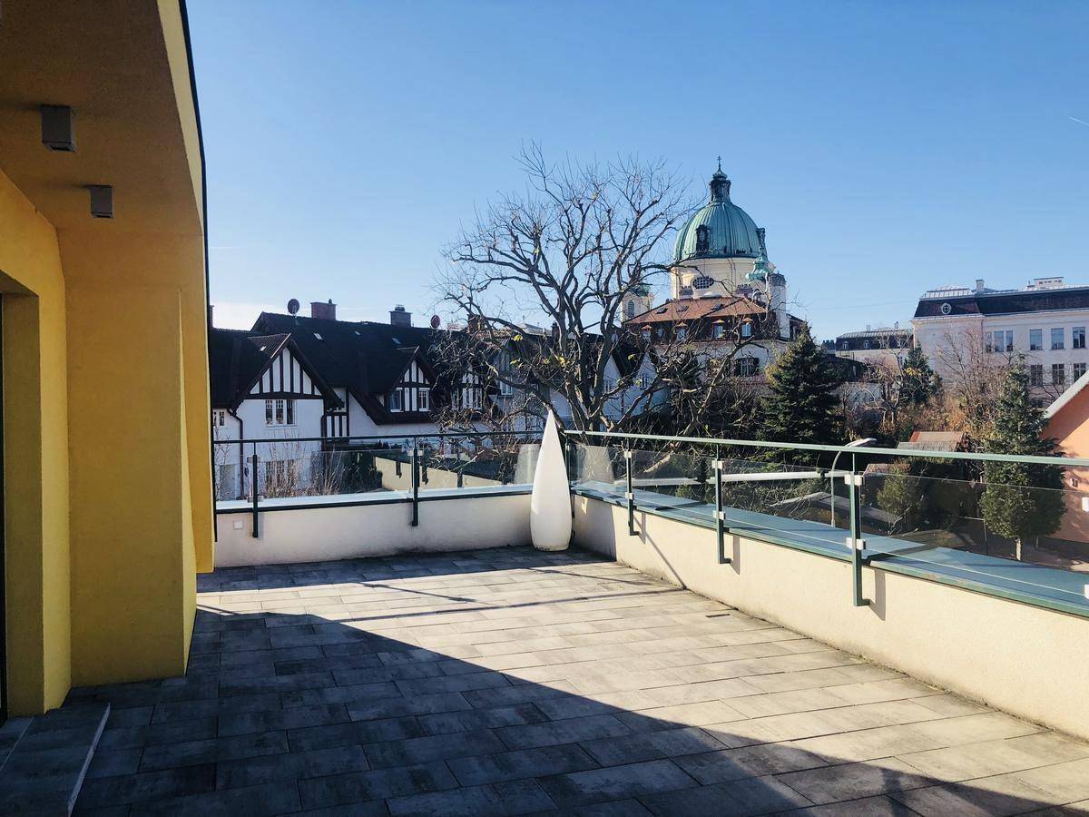Große sonnige Dachterrasse mit Glasgeländer und weitem Blick über die Stadt.