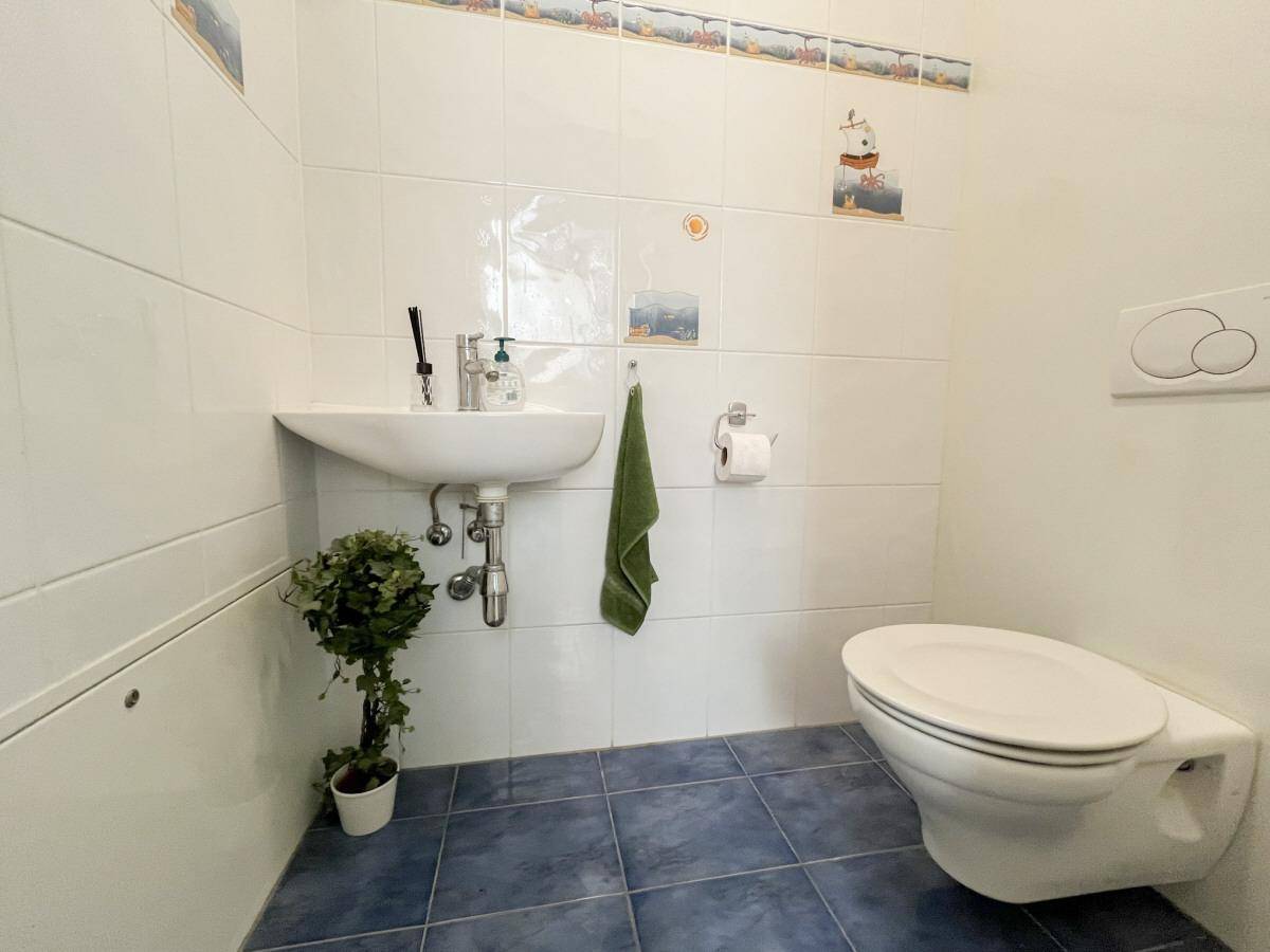 Kleines Gäste-WC mit weißen Fliesen, blauem Boden und Wand-WC.
