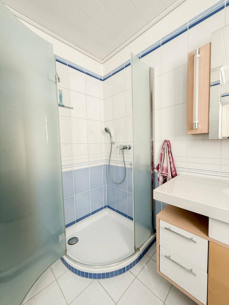 Badezimmer mit Eckdusche, Glasabtrennung und blau-weißen Wandfliesen.