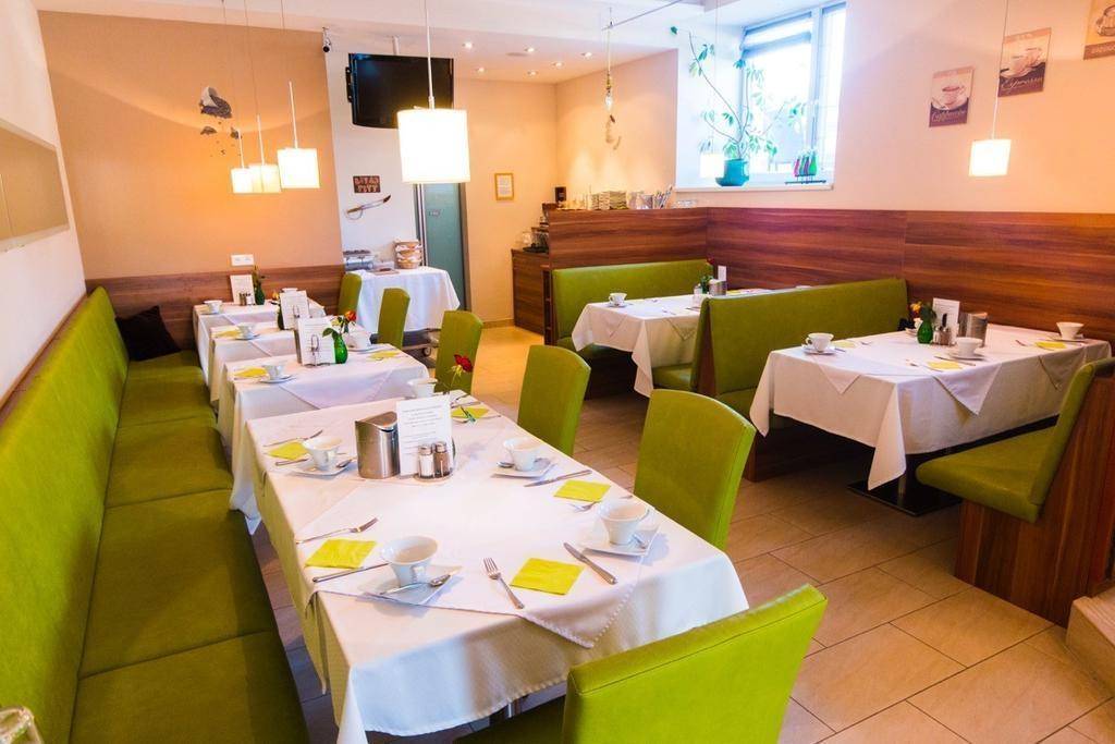 Gemütlicher Speisesaal mit gedeckten Tischen, grünen Sitzbänken und hellem Fliesenboden.