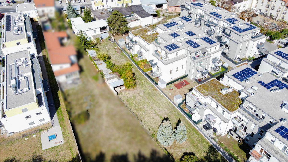 Luftaufnahme eines Grundstücks, umgeben von modernen Wohngebäuden mit Solaranlagen auf den Dächern.