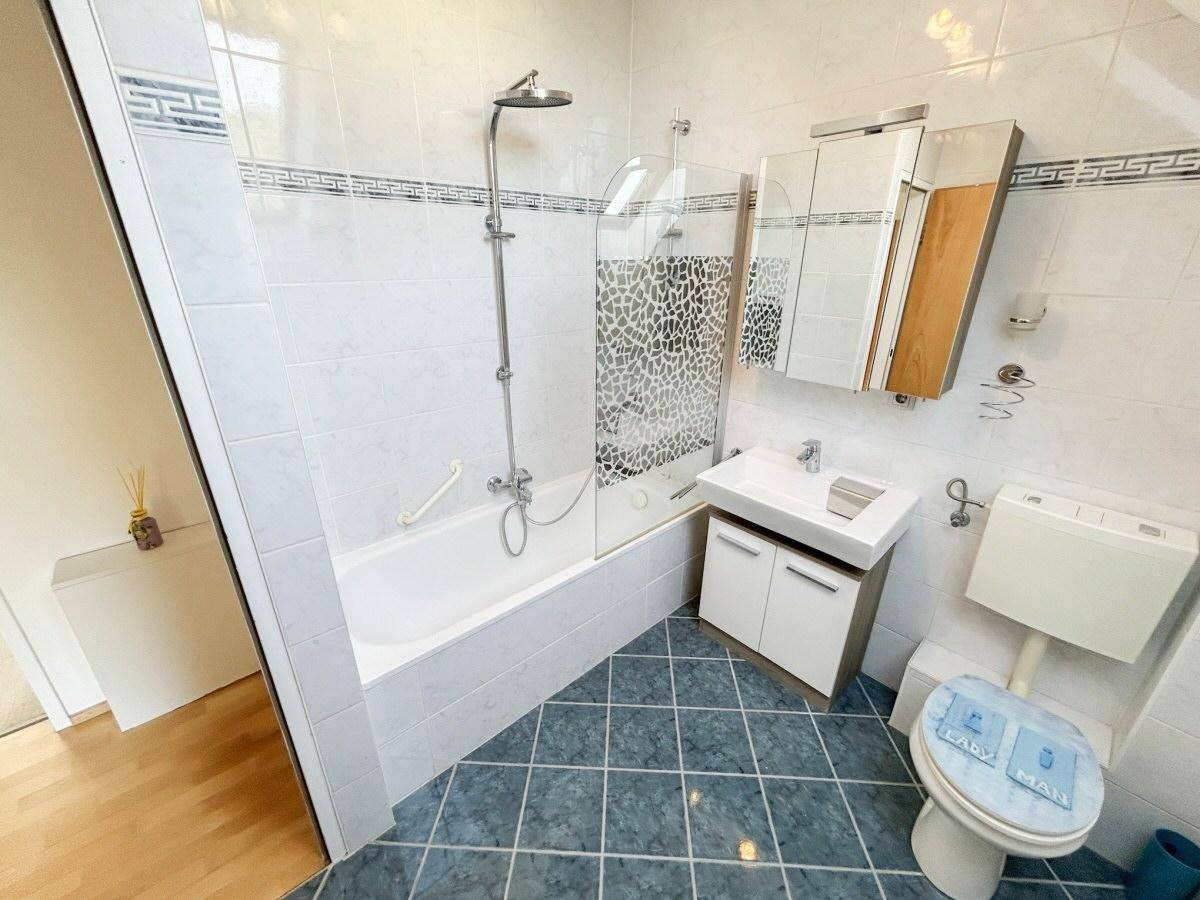 Badezimmer mit Badewanne, Dusche, Waschbecken und blauen Bodenfliesen.