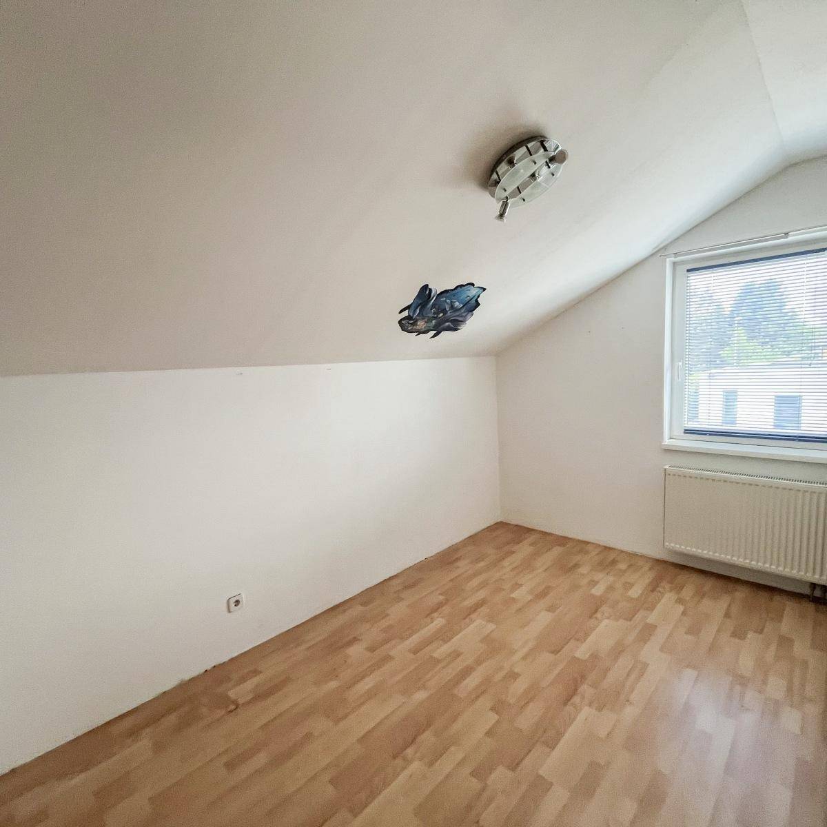 Dachzimmer mit Laminatboden und Fenster, bietet viel natürliches Licht.