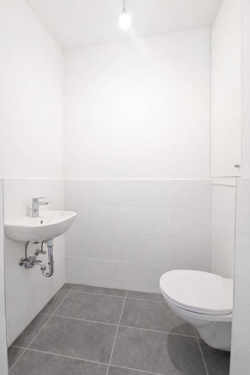 Modernes Gäste-WC mit Wand-WC, kleinem Waschbecken und grauen Bodenfliesen.