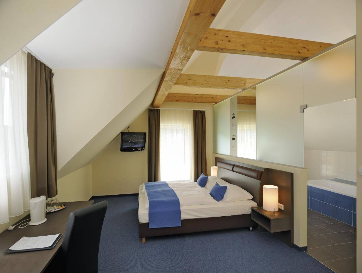 Dachgeschoss-Schlafzimmer mit sichtbaren Holzbalken, blauer Teppichboden und Dachschräge.