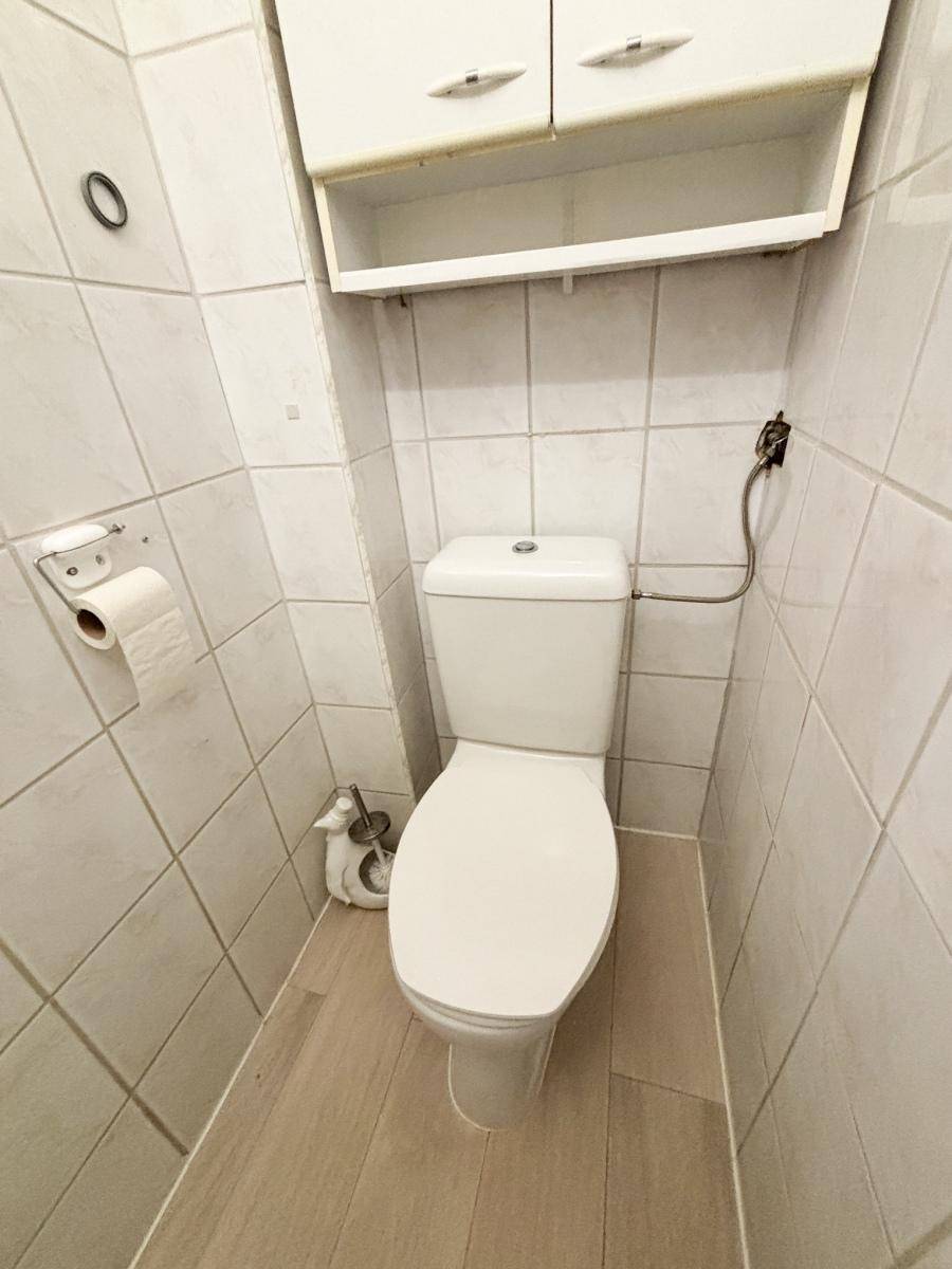 Kleines, gefliestes WC mit Toilette und Hängeschrank, praktisch und funktional.