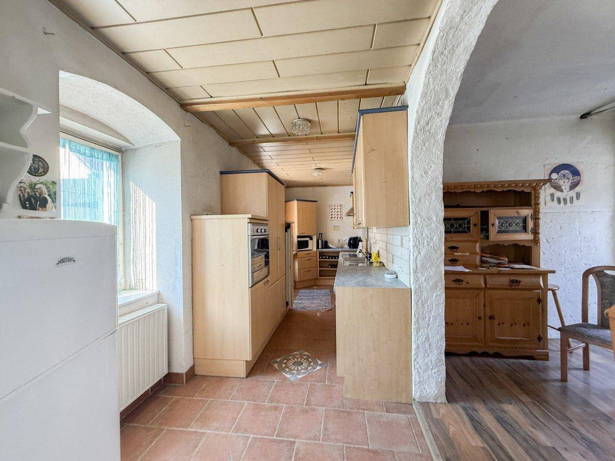 Helle Küche mit Holzschränken, Terrakottafliesen und einem Bogen, der in einen angrenzenden Essbereich führt.