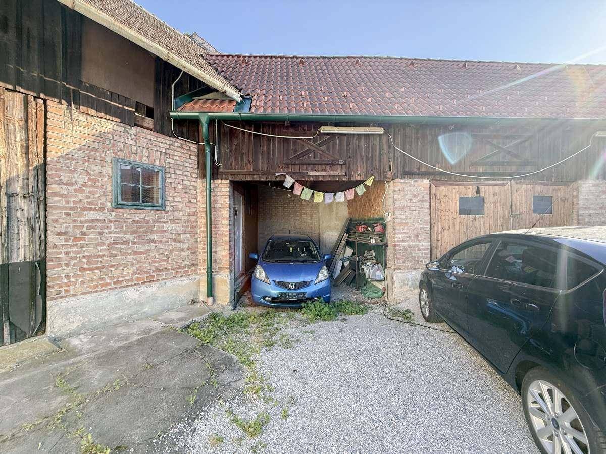 Ländliches Anwesen mit Kiesauffahrt, einem blauen Auto in der offenen Garage und traditionellen Gebäudestrukturen.