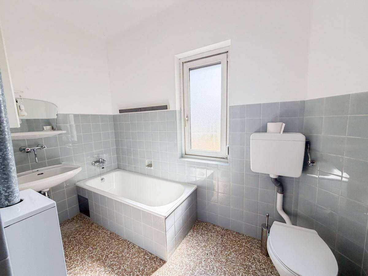 Badezimmer im Stil der 80er Jahre mit blauen Fliesen, Badewanne und Fenster.