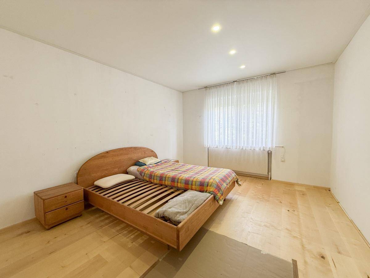Schlafzimmer mit hellem Holzbett, Holzboden und Fenster mit Vorhängen.