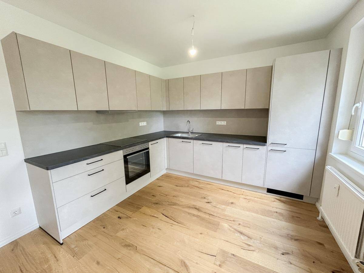 Moderne Einbauküche in hellem Grau mit dunkler Arbeitsplatte und Holzfußboden.